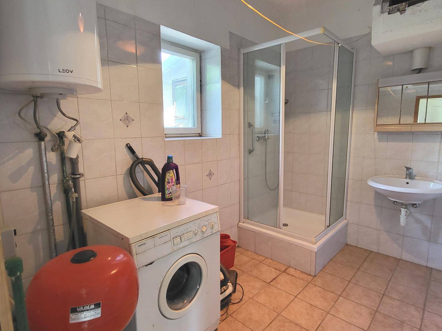 Einfaches Badezimmer oder Hauswirtschaftsraum mit Dusche, Waschmaschine und Warmwasserboiler.