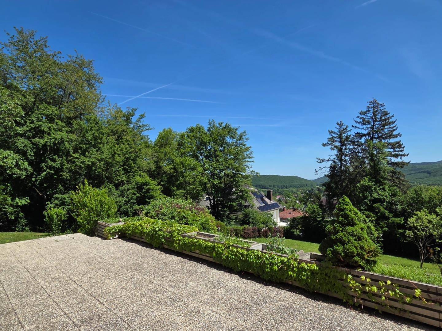 Große gepflasterte Terrasse mit Pflanzenkübeln und weitem Blick über die grüne Landschaft.