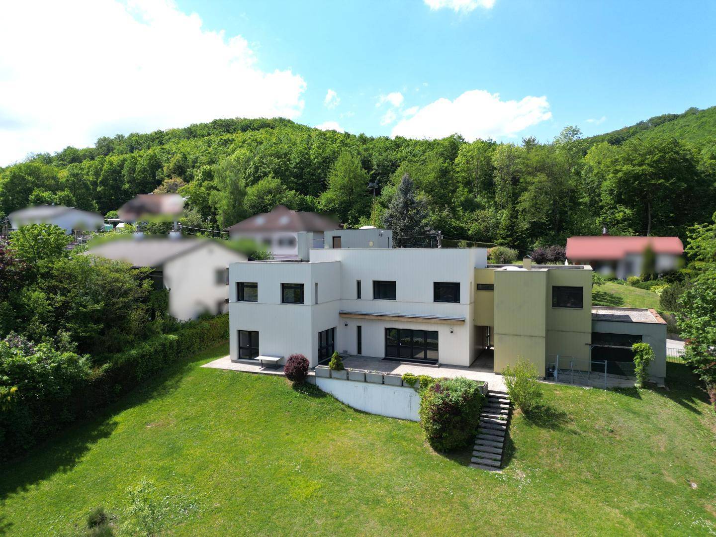 Architektonisch ansprechendes Wohnhaus mit weitläufigem Garten und Blick auf die bewaldeten Hügel.