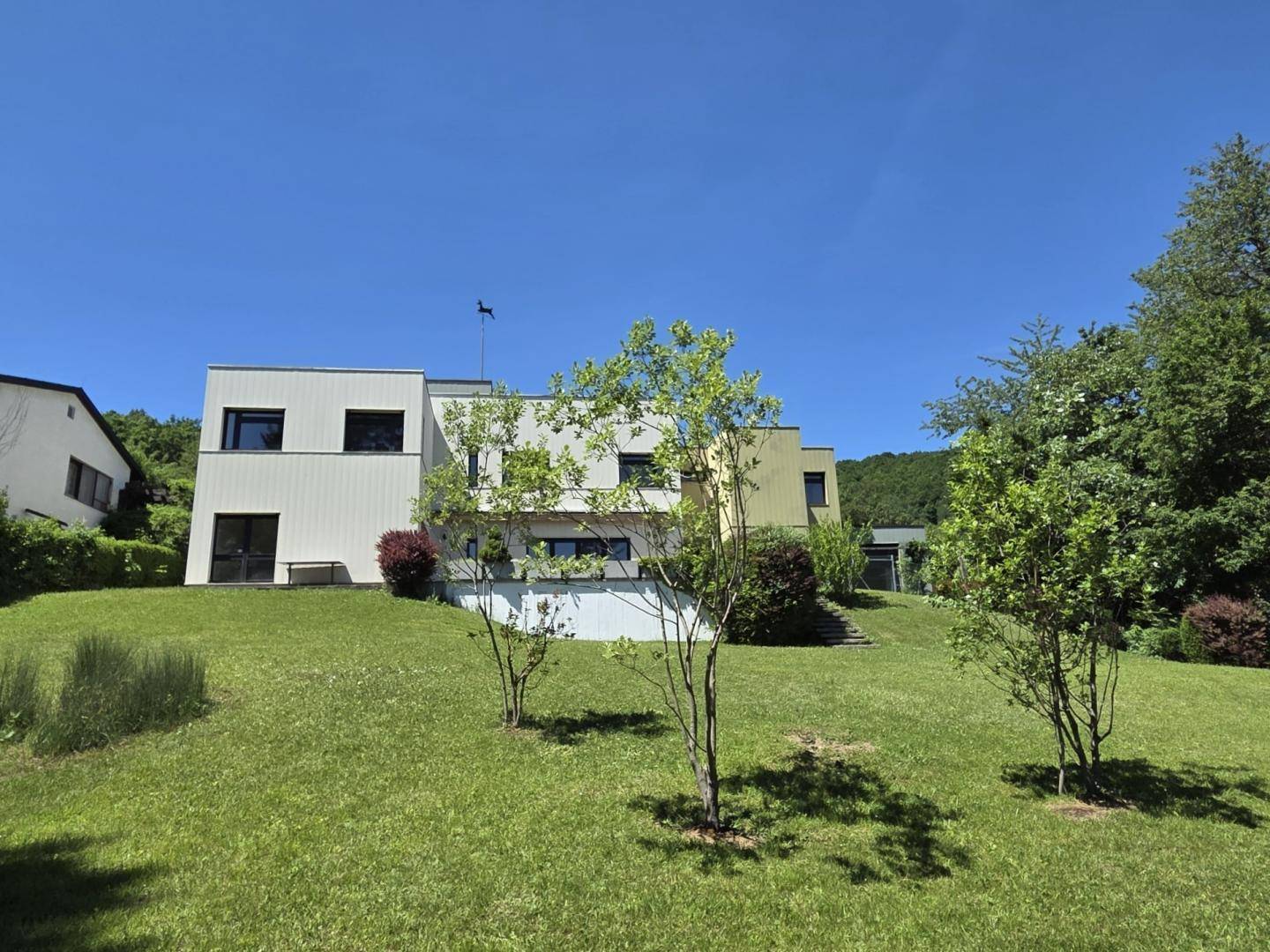 Die moderne Villa präsentiert sich mit einer hellen Fassade und einem gepflegten Vorgarten unter blauem Himmel.