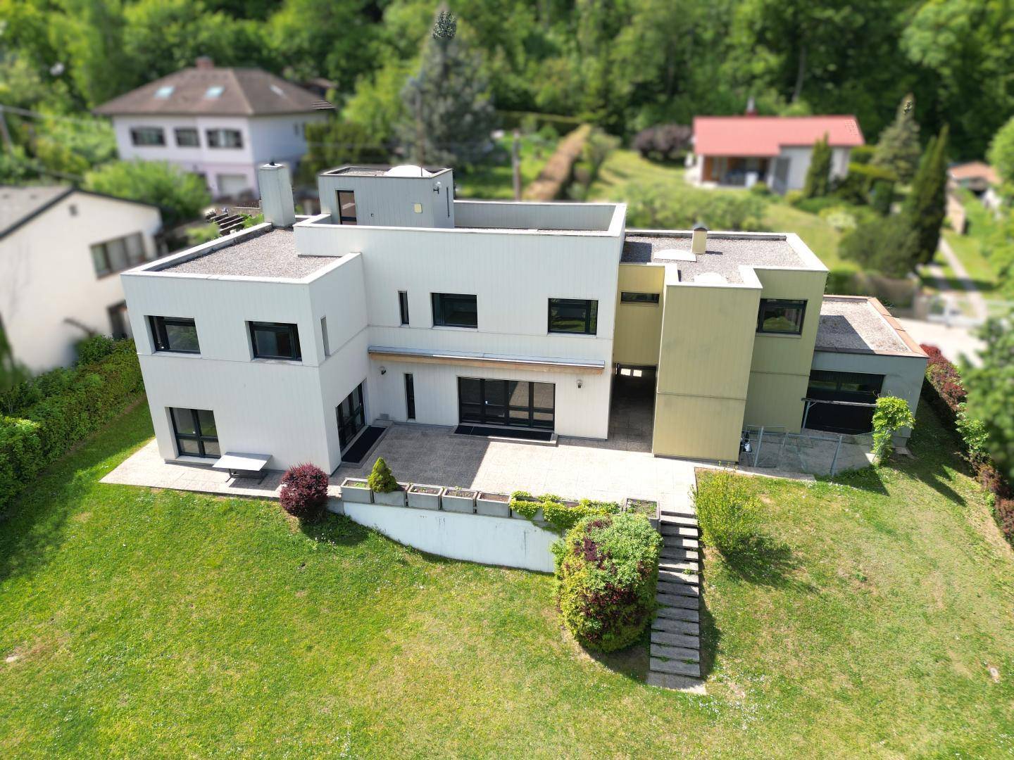 Zeitgenössisches Haus mit mehreren Ebenen und großem Grundstück, eingebettet in eine grüne Umgebung.