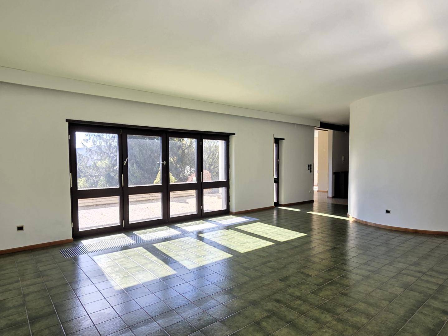 Helles Wohnzimmer mit großen Fenstern und grünem Fliesenboden, bietet Zugang zur Terrasse.