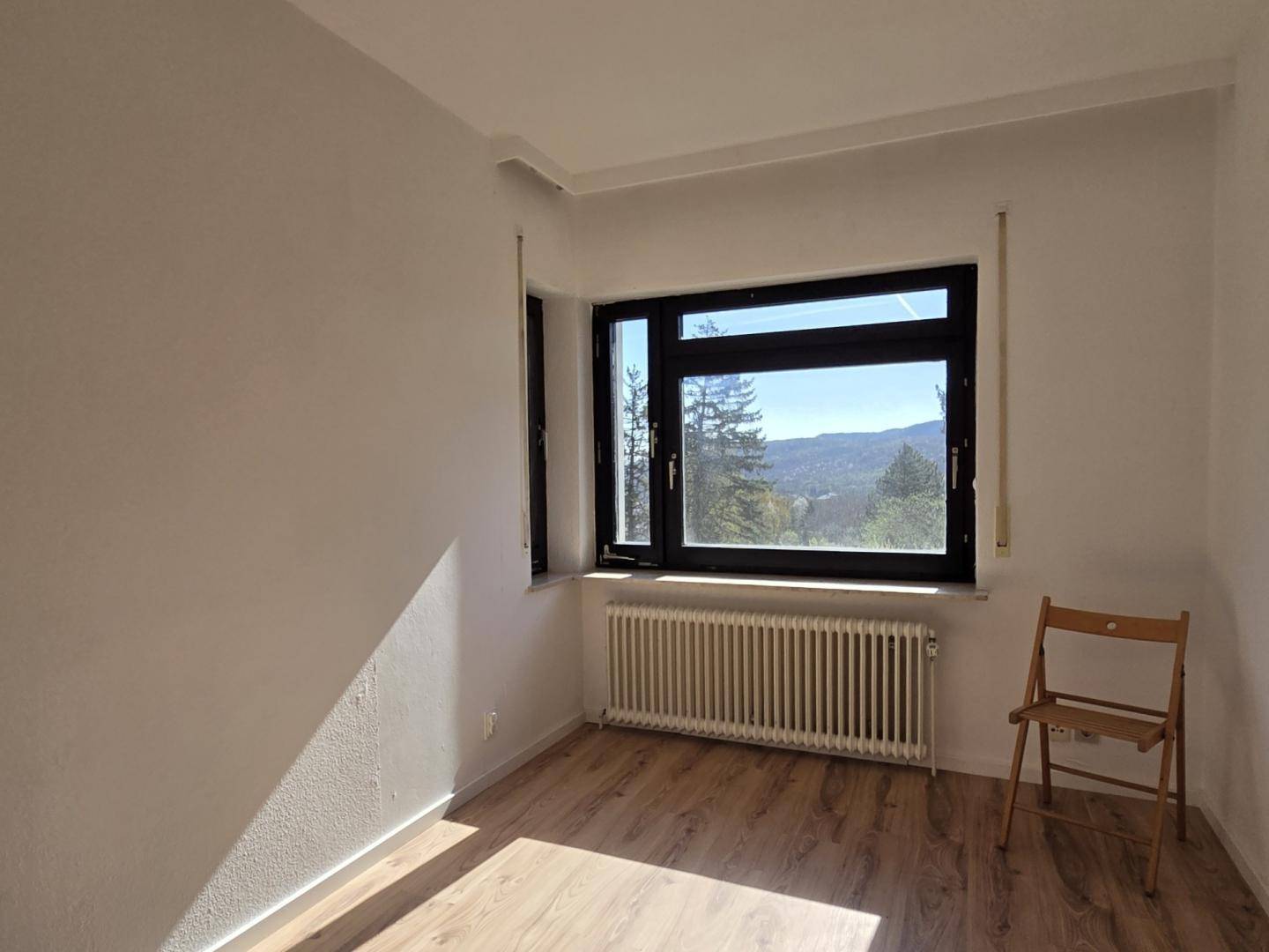 Helles Schlafzimmer mit Laminatboden und großem Fenster, bietet einen weiten Blick ins Grüne.