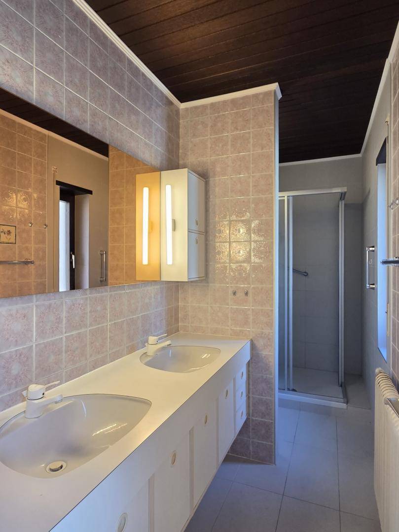 Badezimmer mit Doppelwaschbecken, Duschkabine und gefliesten Wänden, in gutem Zustand.