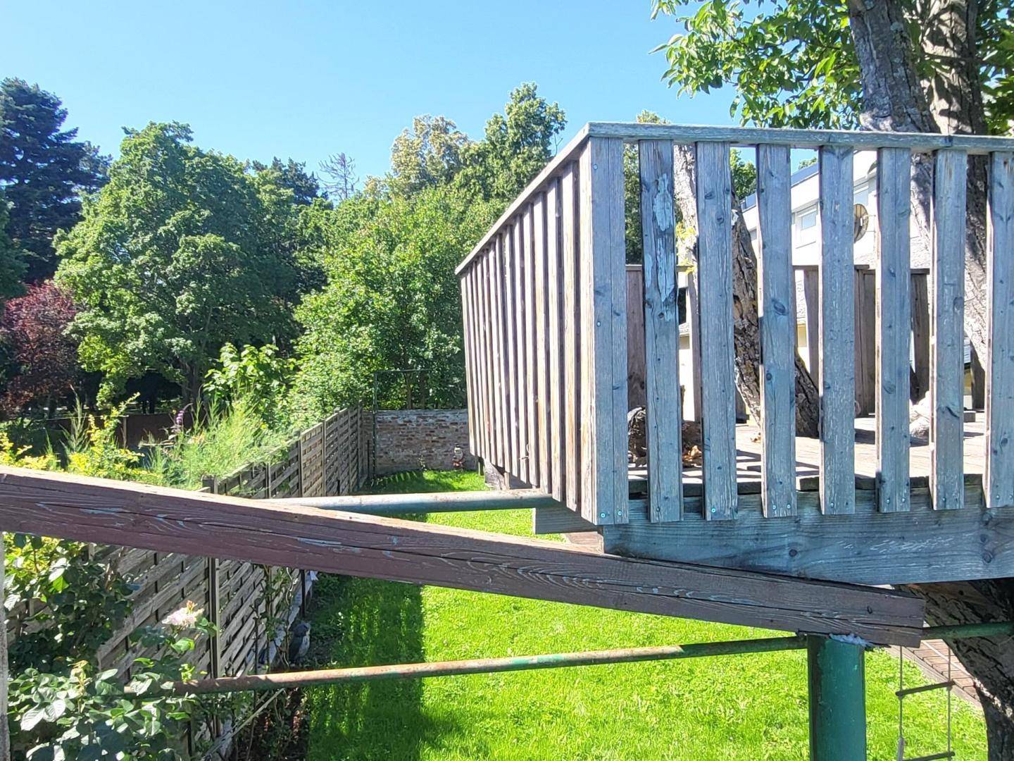 Blick vom Baumhaus auf den grünen Garten mit Rasenfläche und Zaun an einem sonnigen Tag.