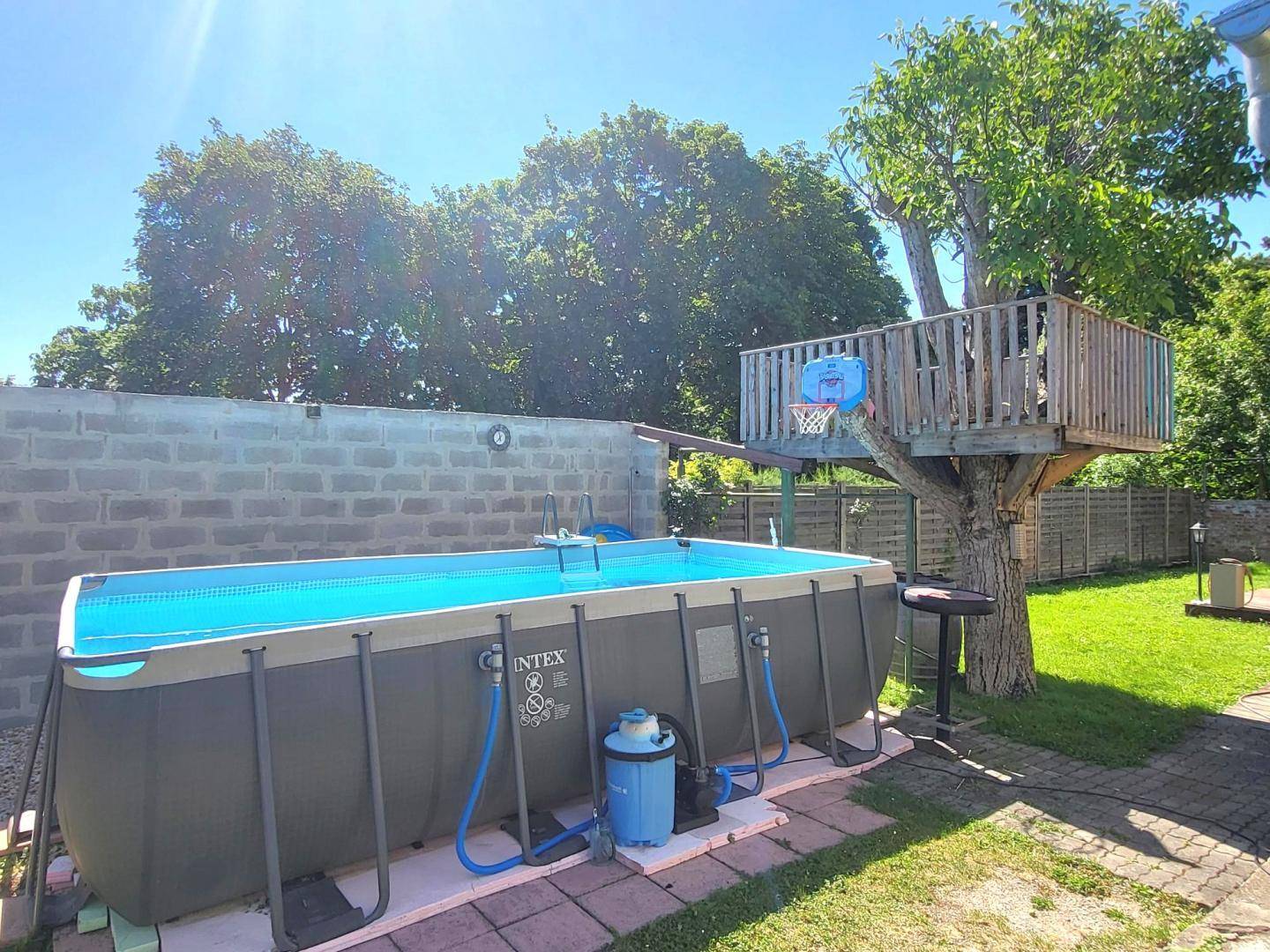 Großer Aufstellpool und Baumhaus mit Basketballkorb im sonnigen Gartenbereich.