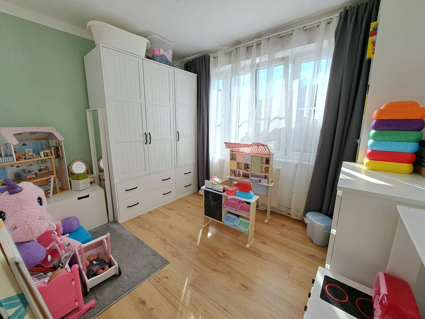 Kinderzimmer mit hellem Holzboden, großem Kleiderschrank und viel natürlichem Licht.