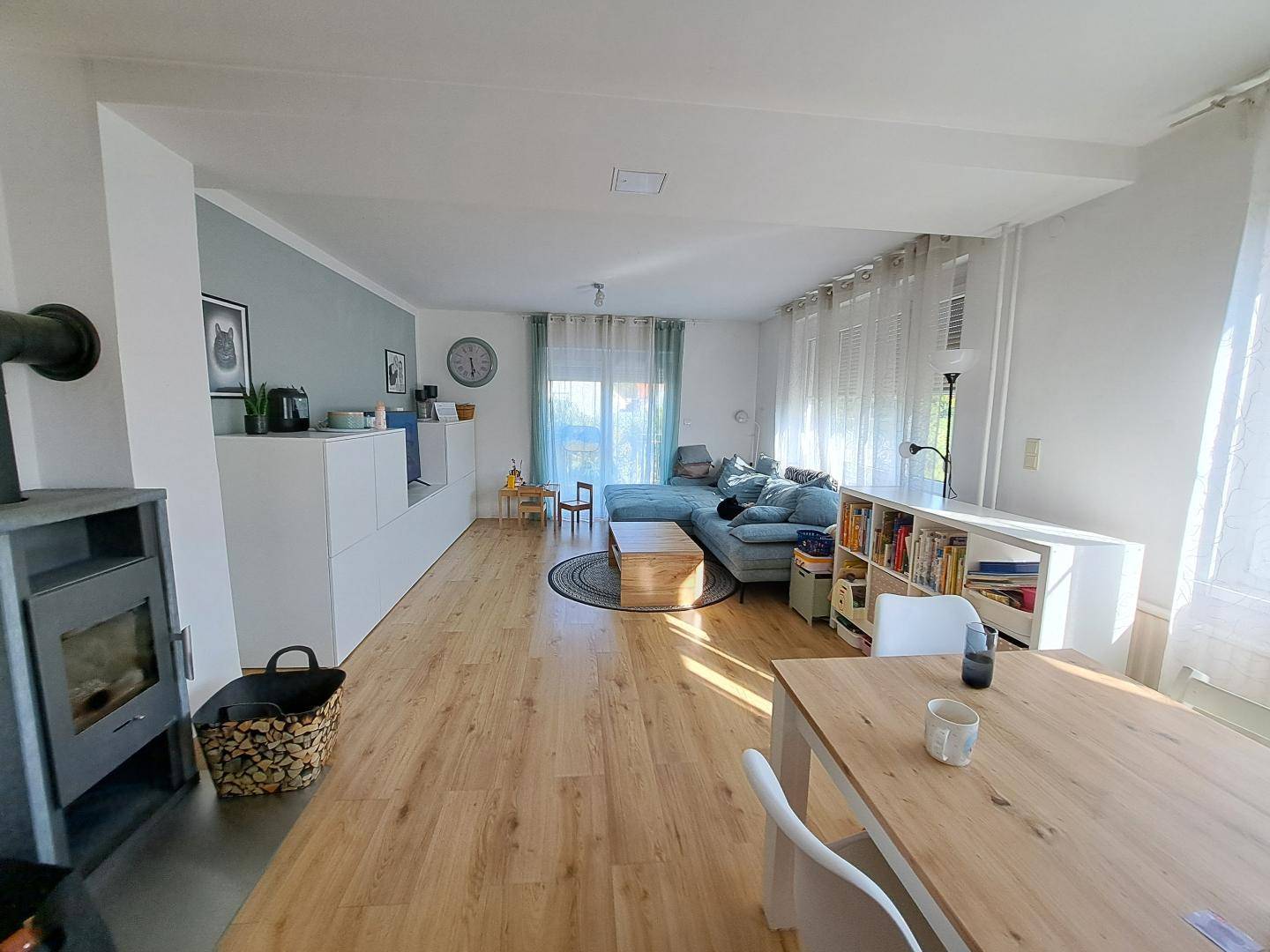 Heller offener Wohn-Essbereich mit Holzboden, Kaminofen und modernem Sofa.