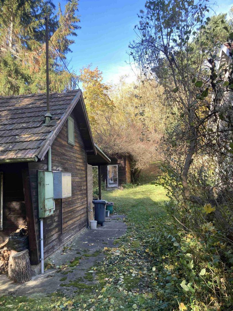 Rustikales Holzhaus mit Ziegeldach und schmalem Weg, umgeben von Bäumen und herbstlicher Vegetation.