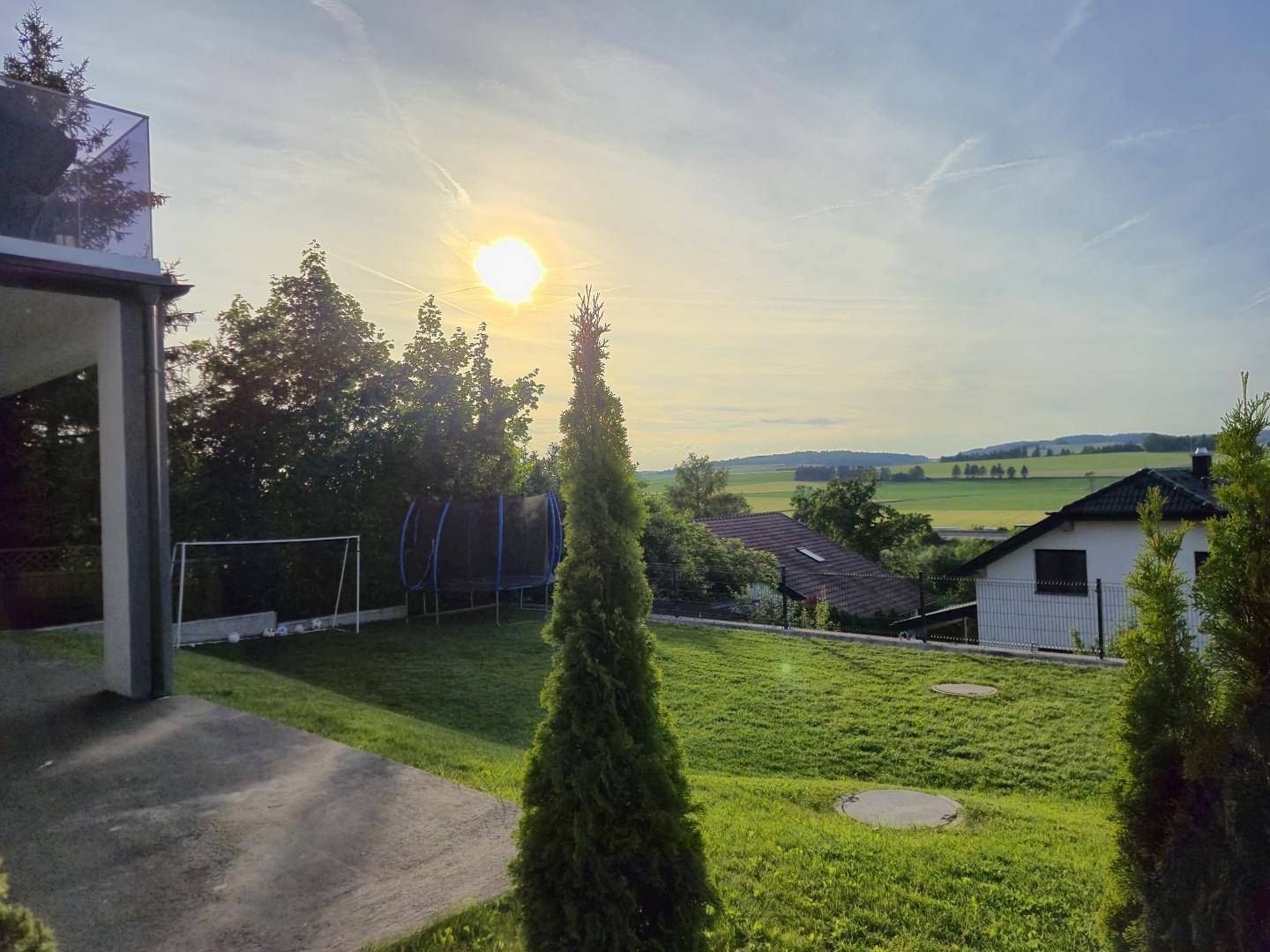 Großer, gepflegter Garten mit Rasenfläche, Trampolin und weitem Blick in die Landschaft.