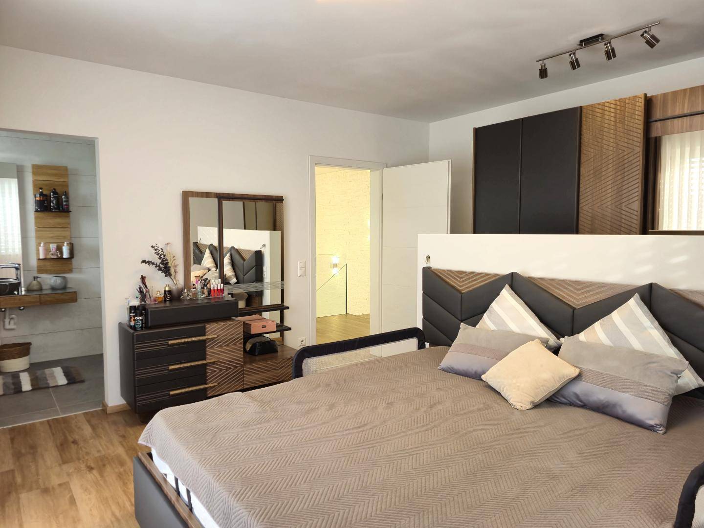 Modernes Schlafzimmer mit großem Bett, Kleiderschrank und Zugang zu einem angrenzenden Bad.