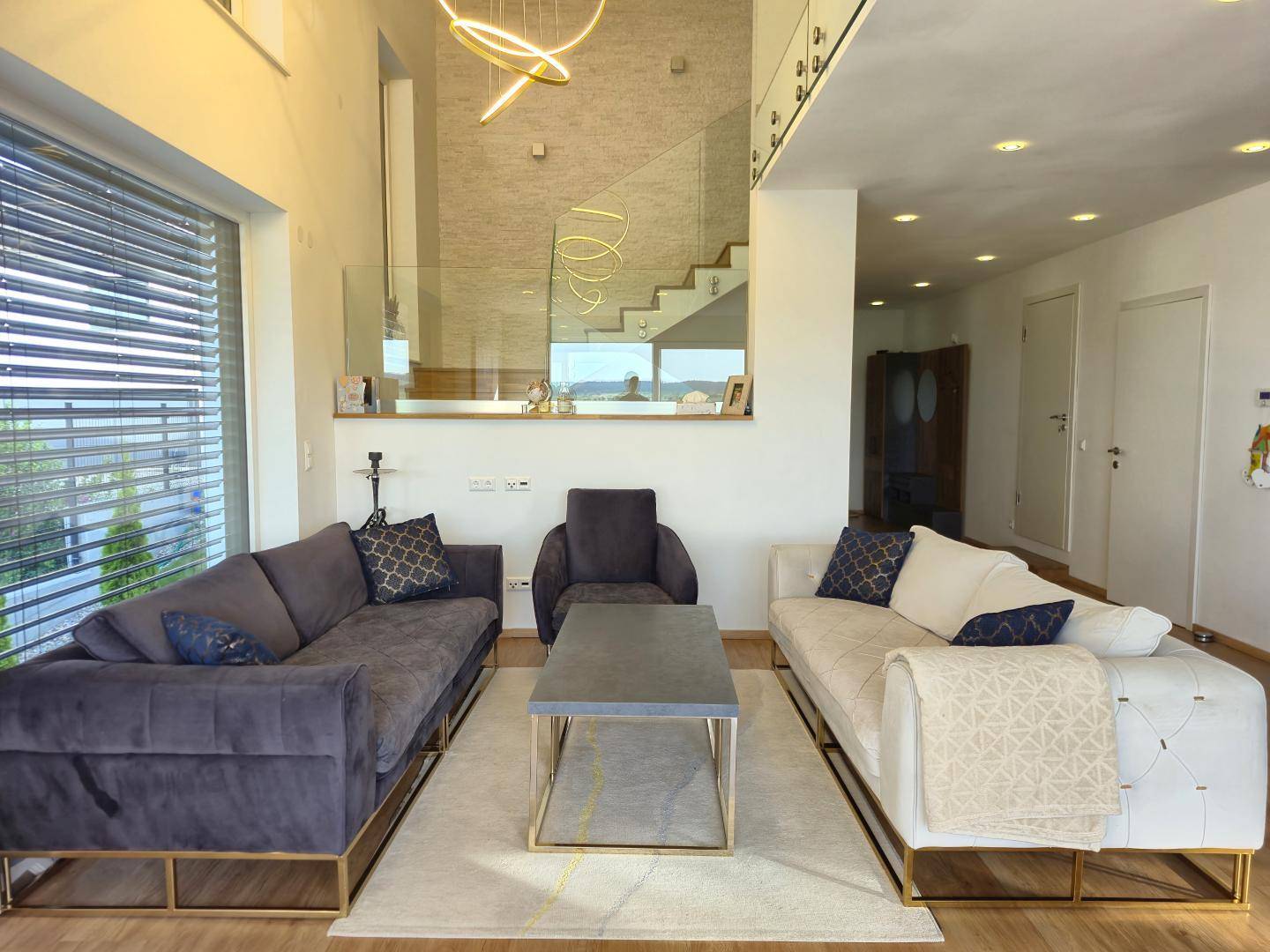 Geräumiges Wohnzimmer mit hohen Decken, großen Fenstern und moderner Einrichtung.