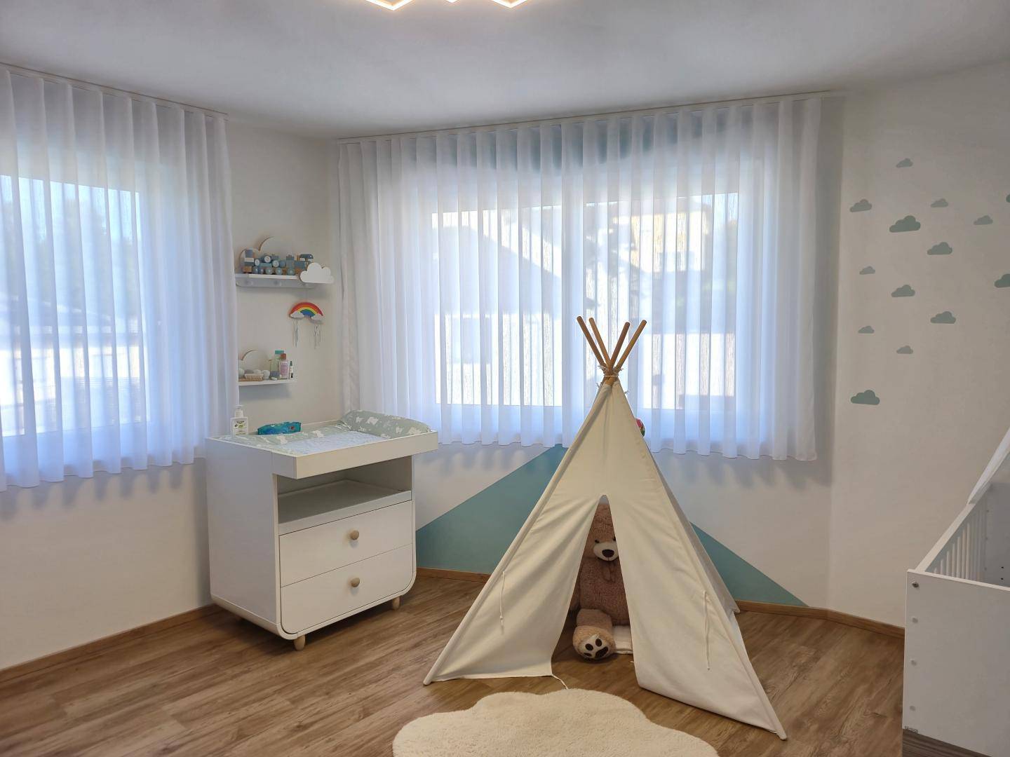 Helles Kinderzimmer mit Wickeltisch, Spielzelt und freundlicher Wandgestaltung.