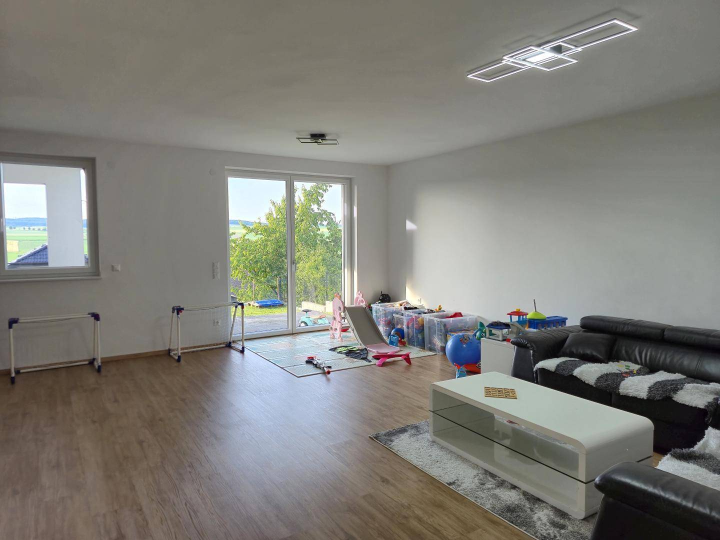 Helles Wohnzimmer mit Holzboden, großen Schiebetüren und einem weiten Blick ins Grüne.
