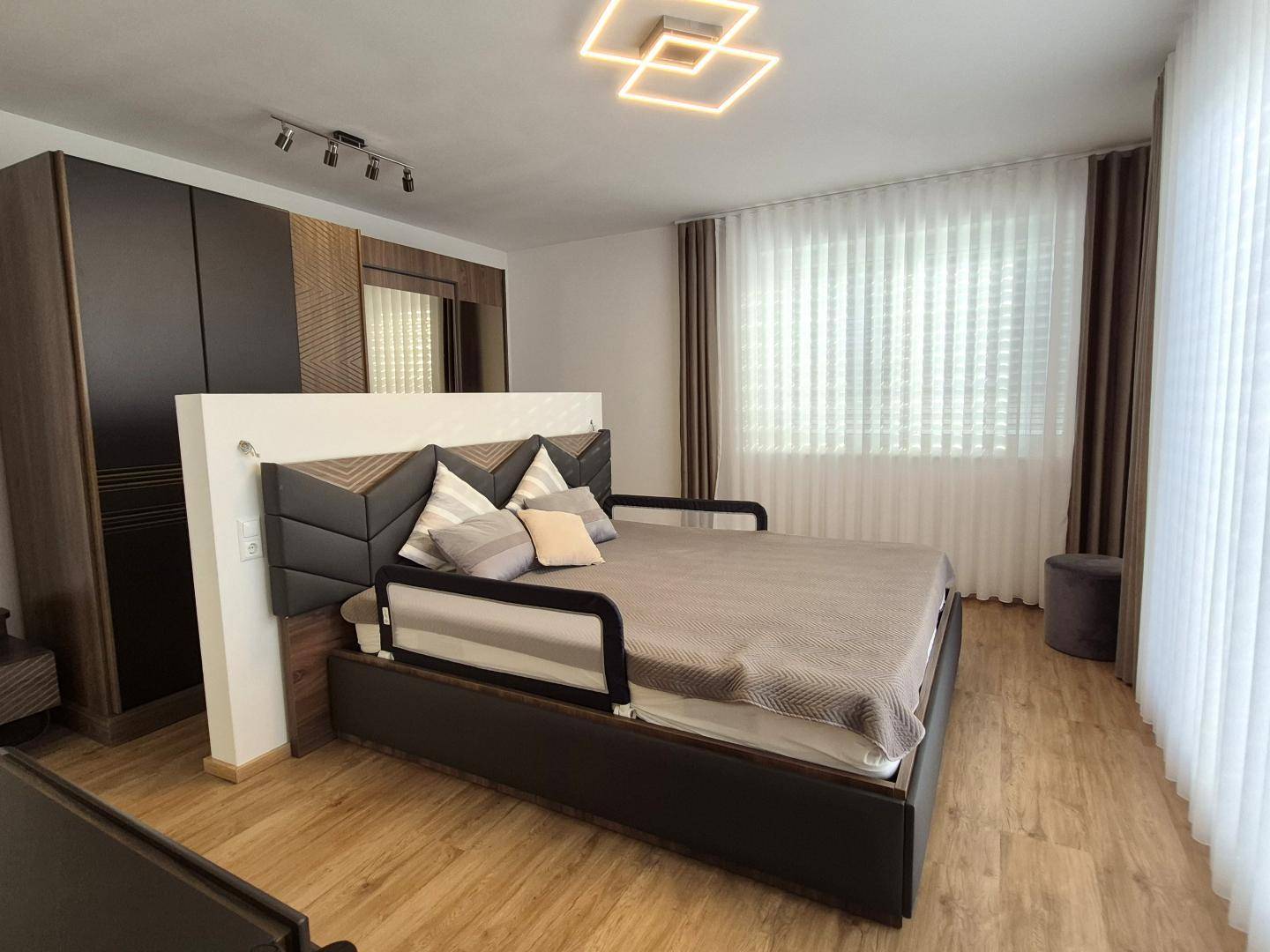 Gemütliches Schlafzimmer mit großem Doppelbett, Kleiderschrank und hellen Vorhängen.
