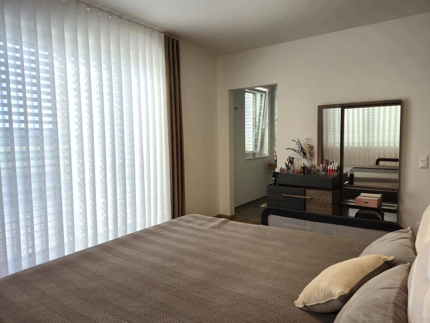 Schlafzimmer mit großem Fenster, modernem Bett und Blick auf das angrenzende Badezimmer.