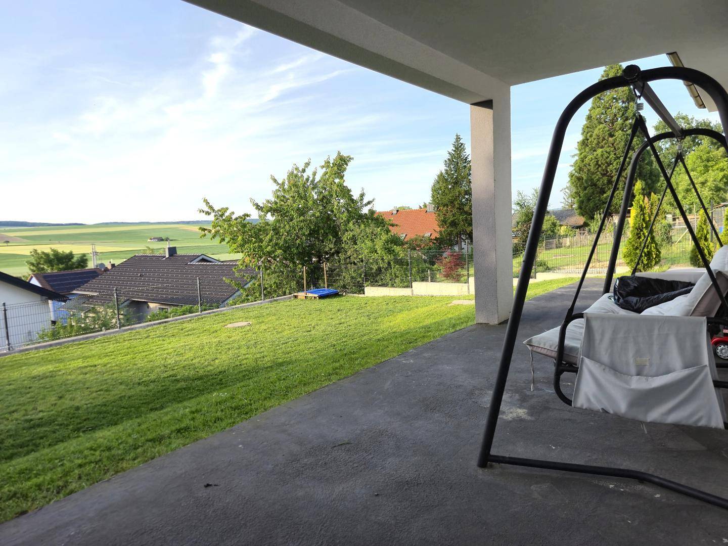 Überdachte Terrasse mit Schaukel und weitem Blick über die grüne Landschaft und umliegende Häuser.