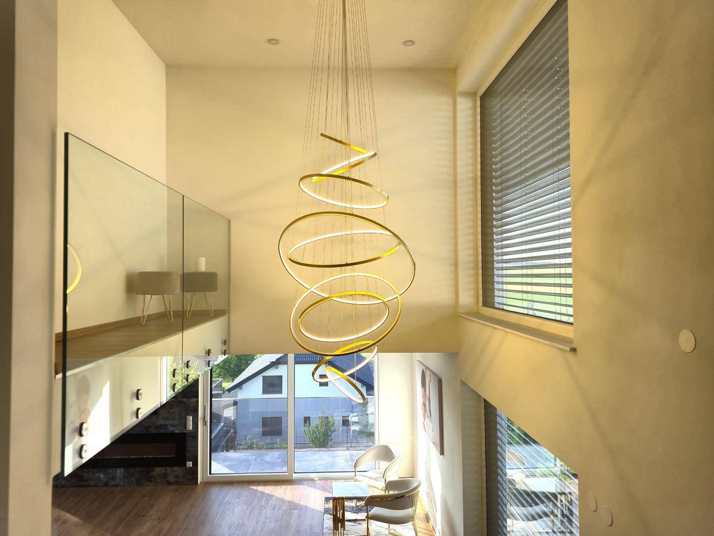 Moderner Eingangsbereich mit hoher Decke, eleganter Hängeleuchte und Glasgeländer, das viel Licht hereinlässt.