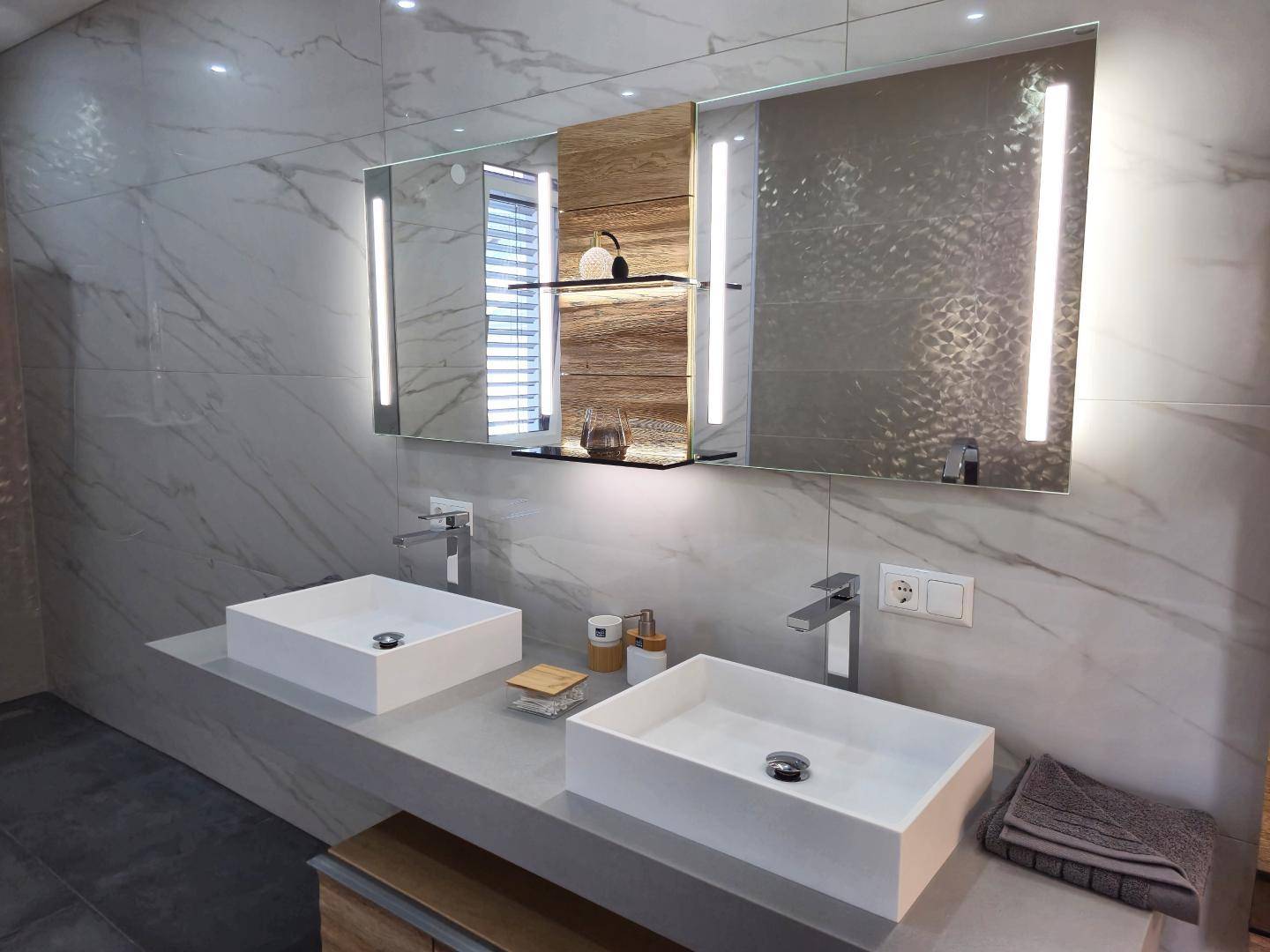 Modernes Badezimmer mit Doppelwaschbecken, beleuchtetem Spiegel und eleganten Fliesen.
