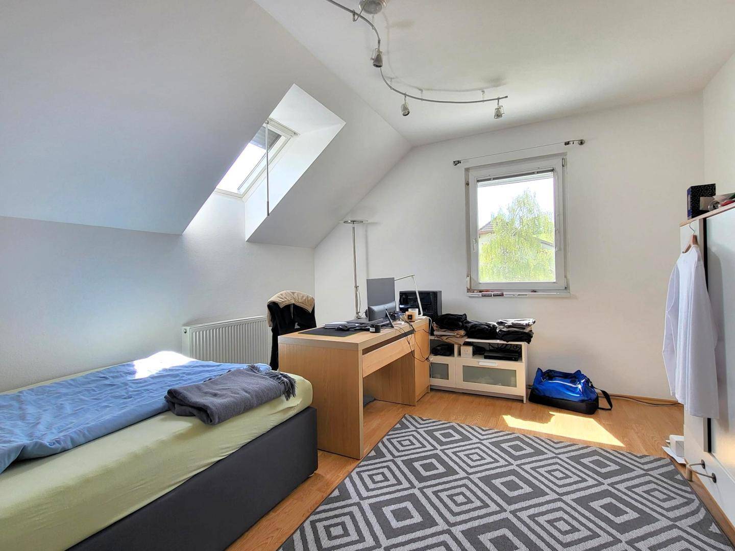 Geräumiges Zimmer im Dachgeschoss mit Bett, Schreibtisch und Dachfenster.