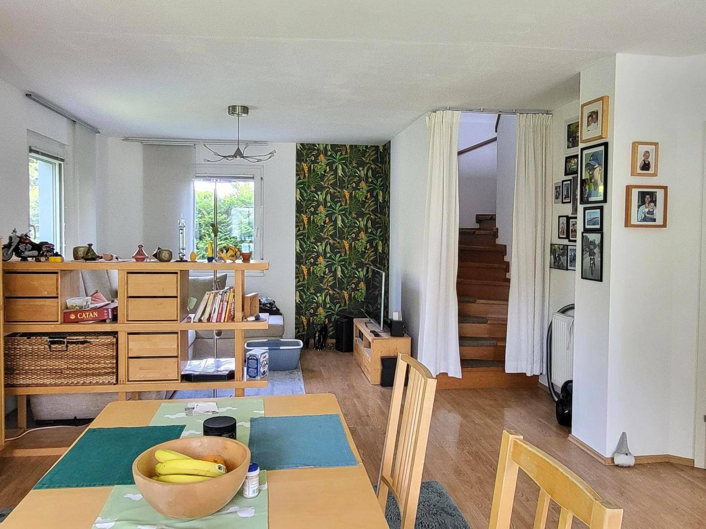 Geräumiger Wohn- und Essbereich mit Holzboden, dekorativer Tapete und Treppenzugang.