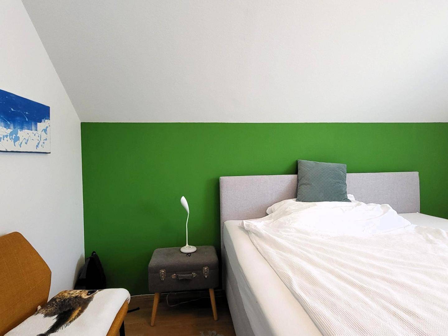 Schlafzimmer im Dachgeschoss mit grüner Akzentwand, Bett und schräger Decke.
