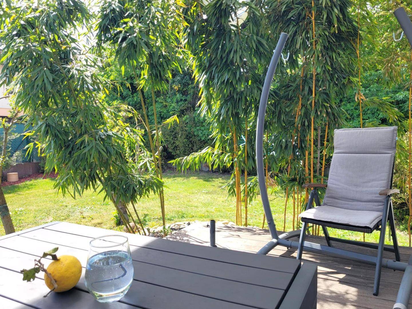 Gemütliche Holzterrasse mit Gartenmöbeln und üppiger Bambusbepflanzung im Hintergrund.
