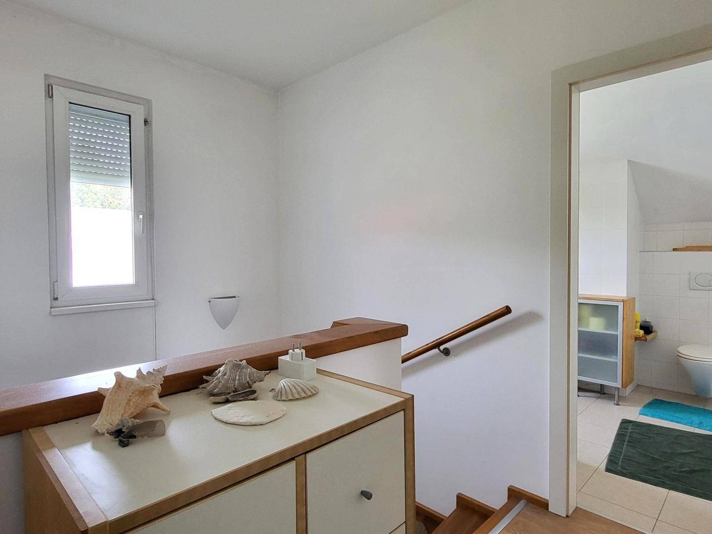 Heller Treppenabsatz mit Fenster und dekorativen Muscheln auf einer Kommode.