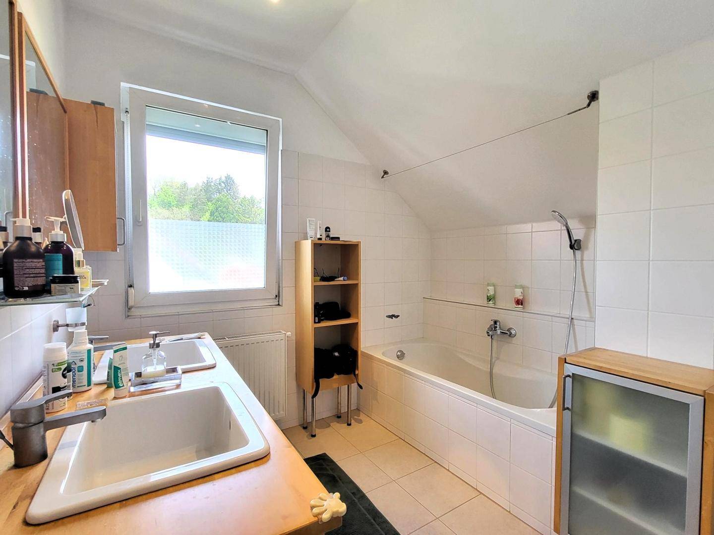 Badezimmer im Dachgeschoss mit Badewanne, Doppelwaschbecken und Fenster mit Ausblick.