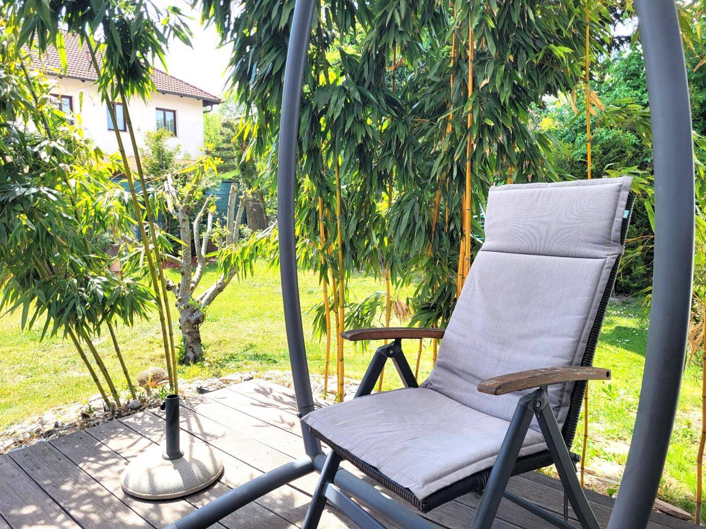 Gemütlicher Sitzbereich auf der Holzterrasse mit einem Liegestuhl und Bambuspflanzen.