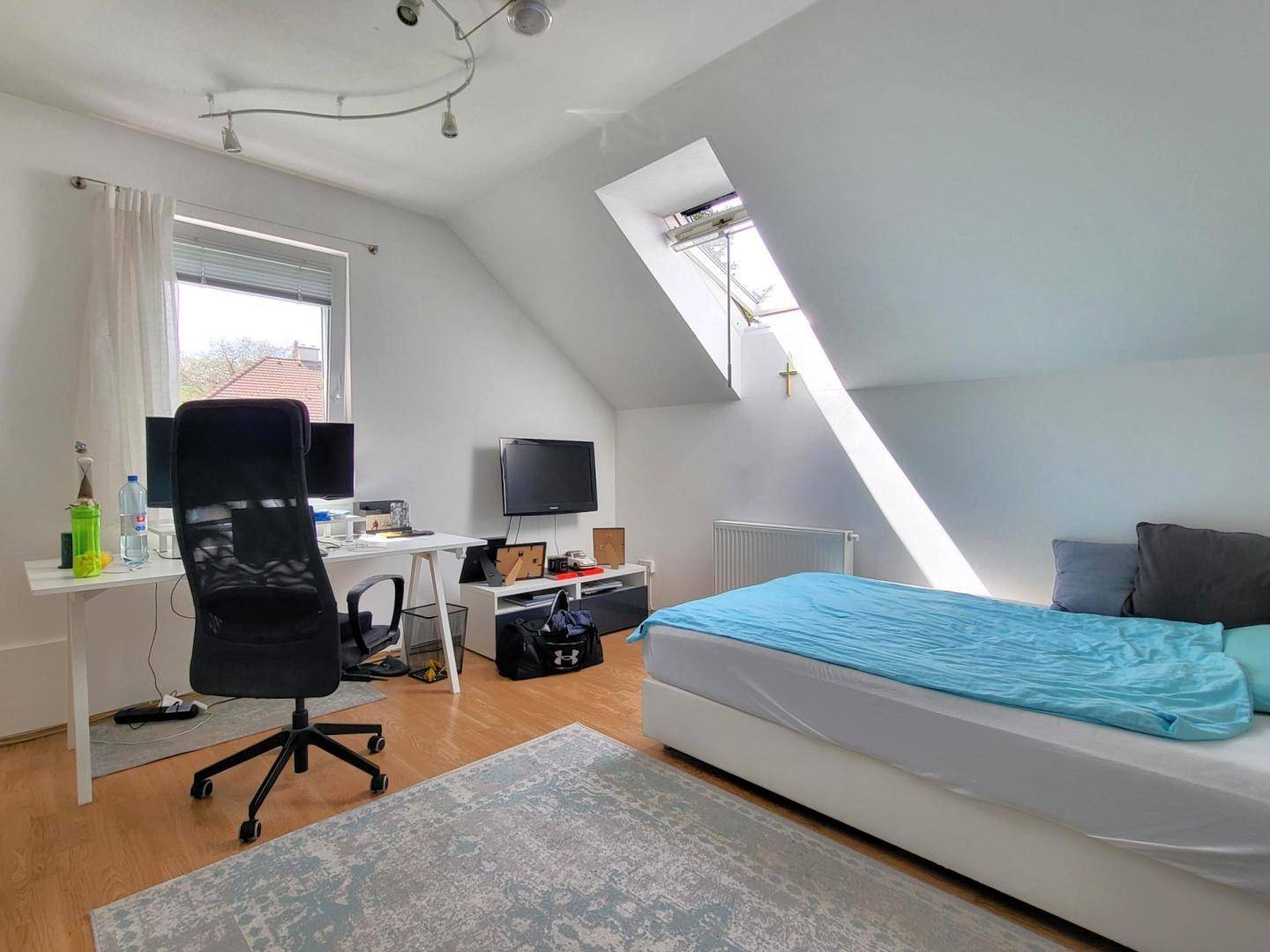 Helles Zimmer im Dachgeschoss mit Schreibtisch, Bett und Dachfenster für viel Licht.
