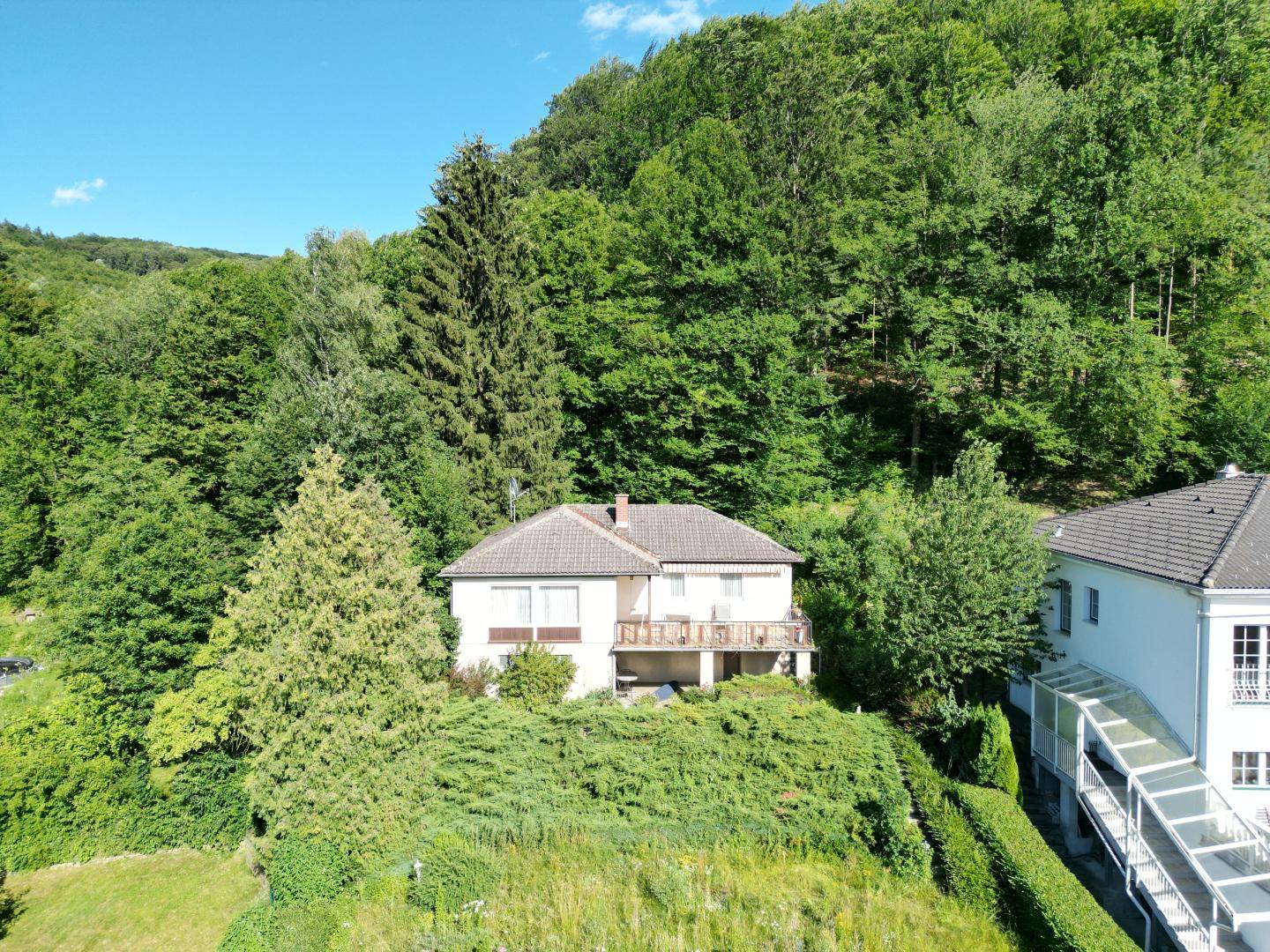 Haus mit Balkon und Blick auf die bewaldete Umgebung, neben einem Nachbargebäude.