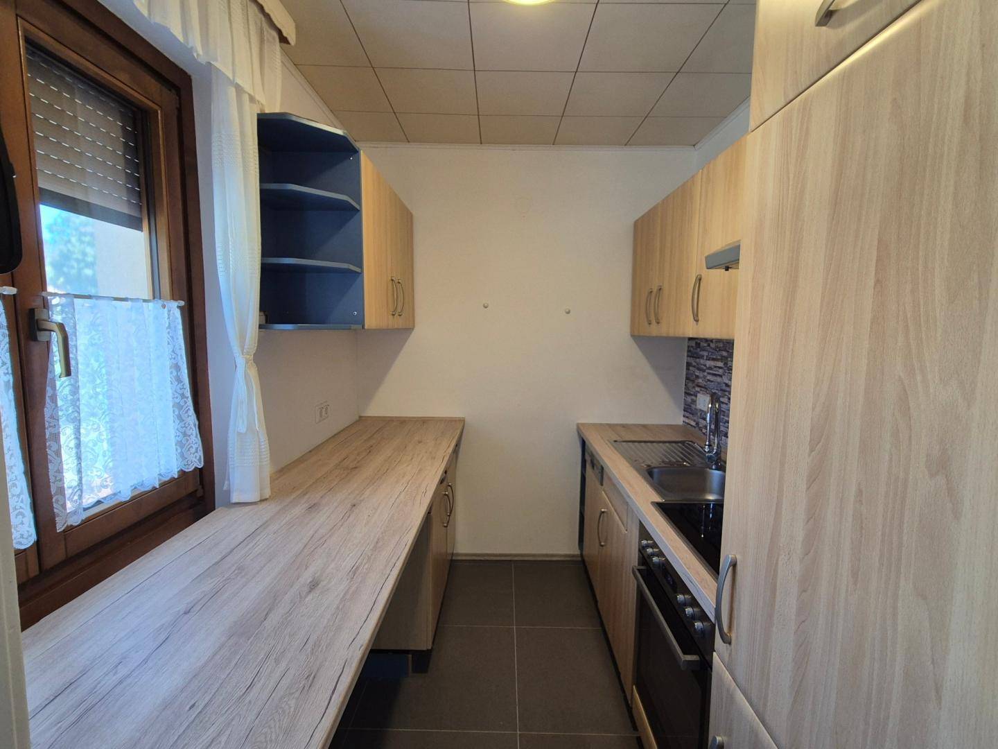 Schmale Küche mit hellen Holzschränken, Arbeitsplatte in Holzoptik und einem Fenster.