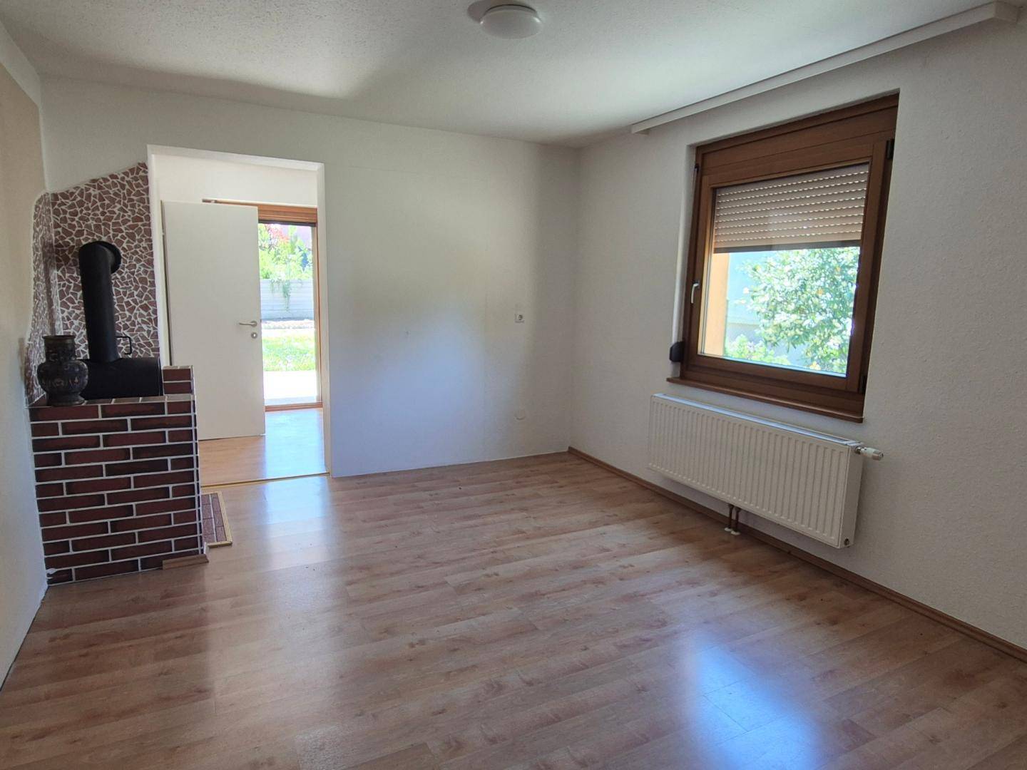 Geräumiges Wohnzimmer mit Laminatboden, Holzofen und Zugang zum Außenbereich durch eine Tür.