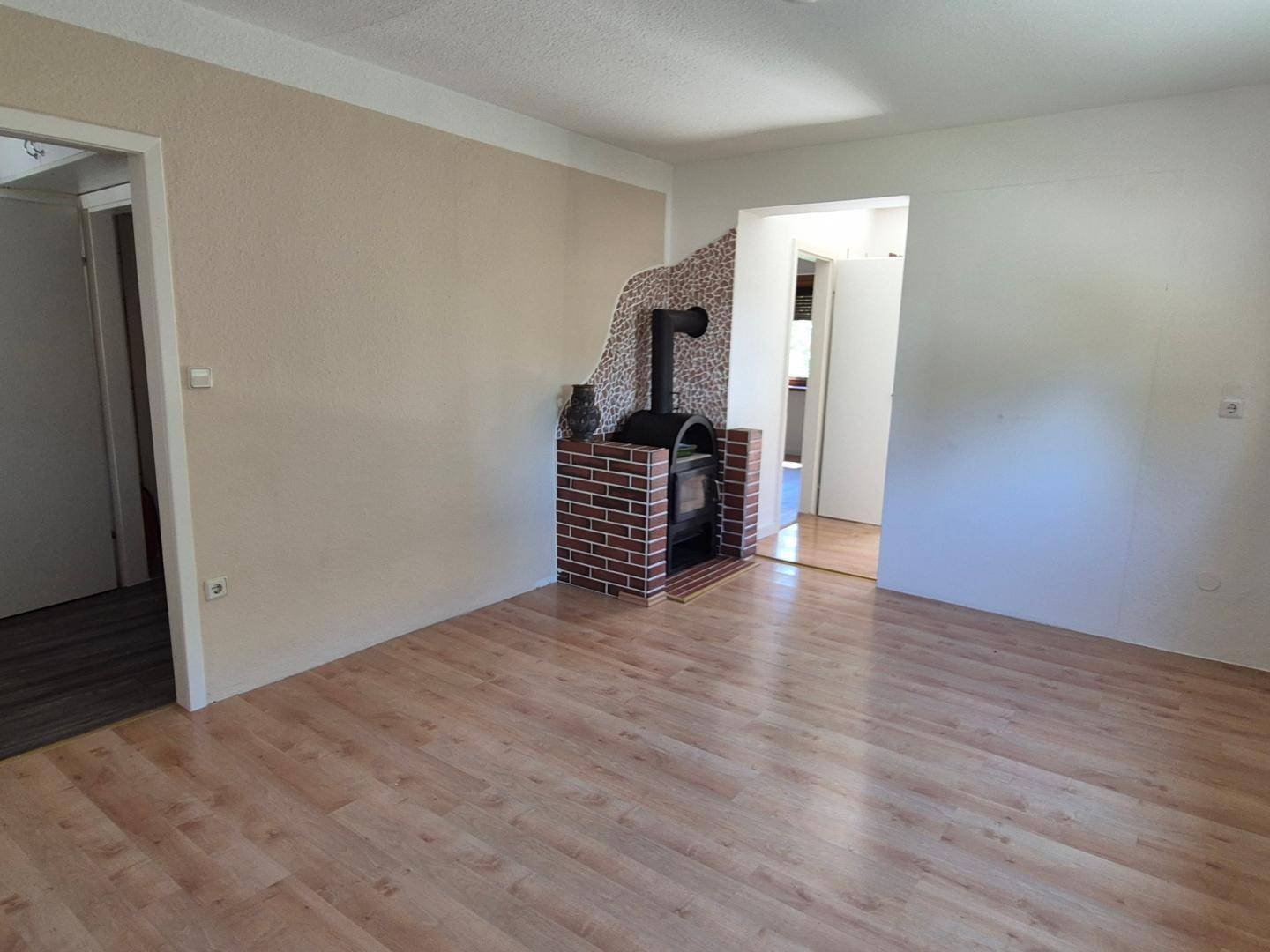 Wohnzimmer mit Laminatboden, hellem Anstrich und einem gemauerten Holzofen als Blickfang.
