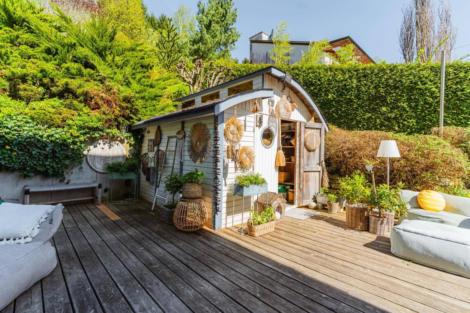 Charmantes Gartenhaus auf einer Holzterrasse, liebevoll dekoriert und von Pflanzen umgeben.