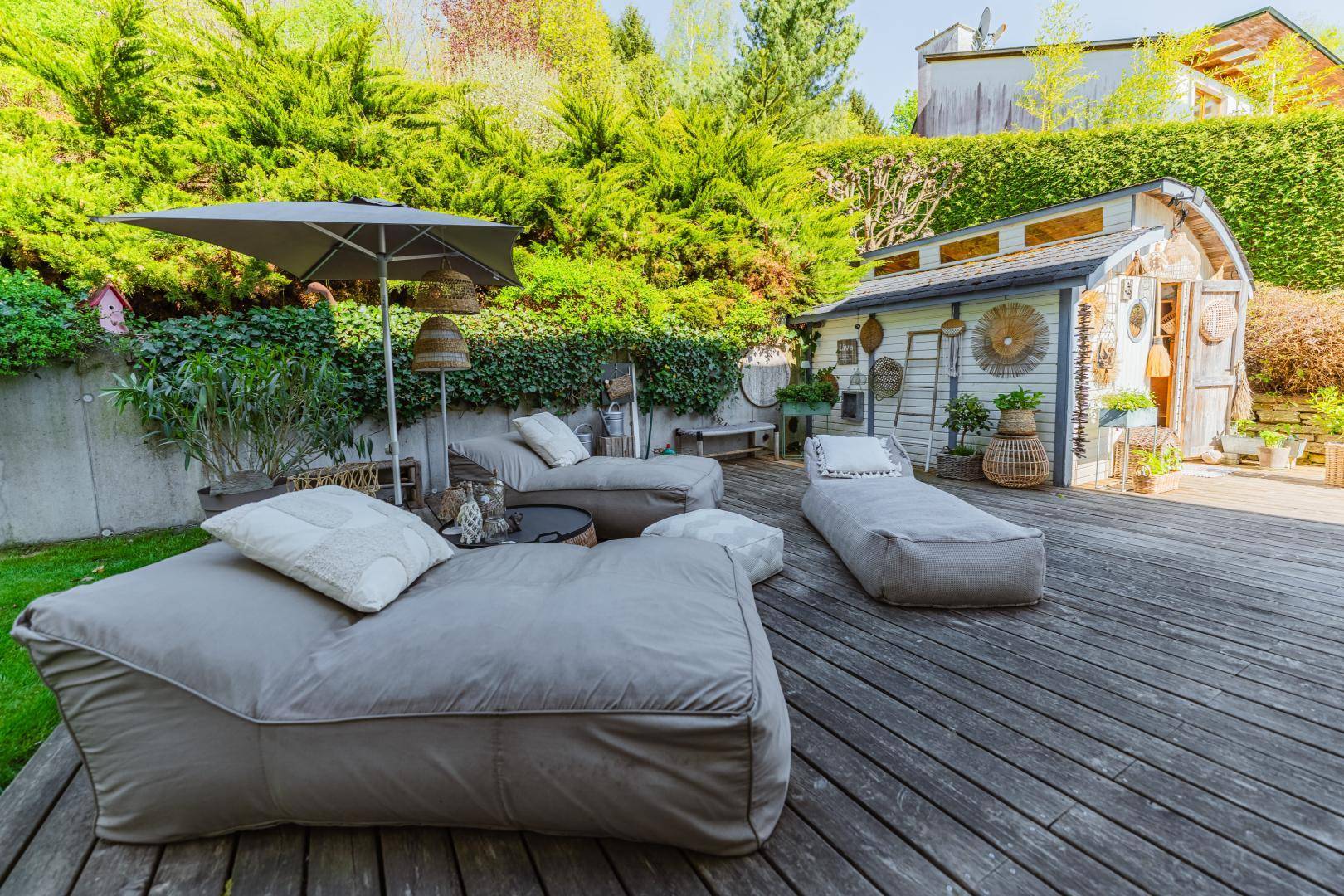 Holzterrasse mit bequemen Liegen und einem charmanten Gartenhaus, umgeben von viel Grün.