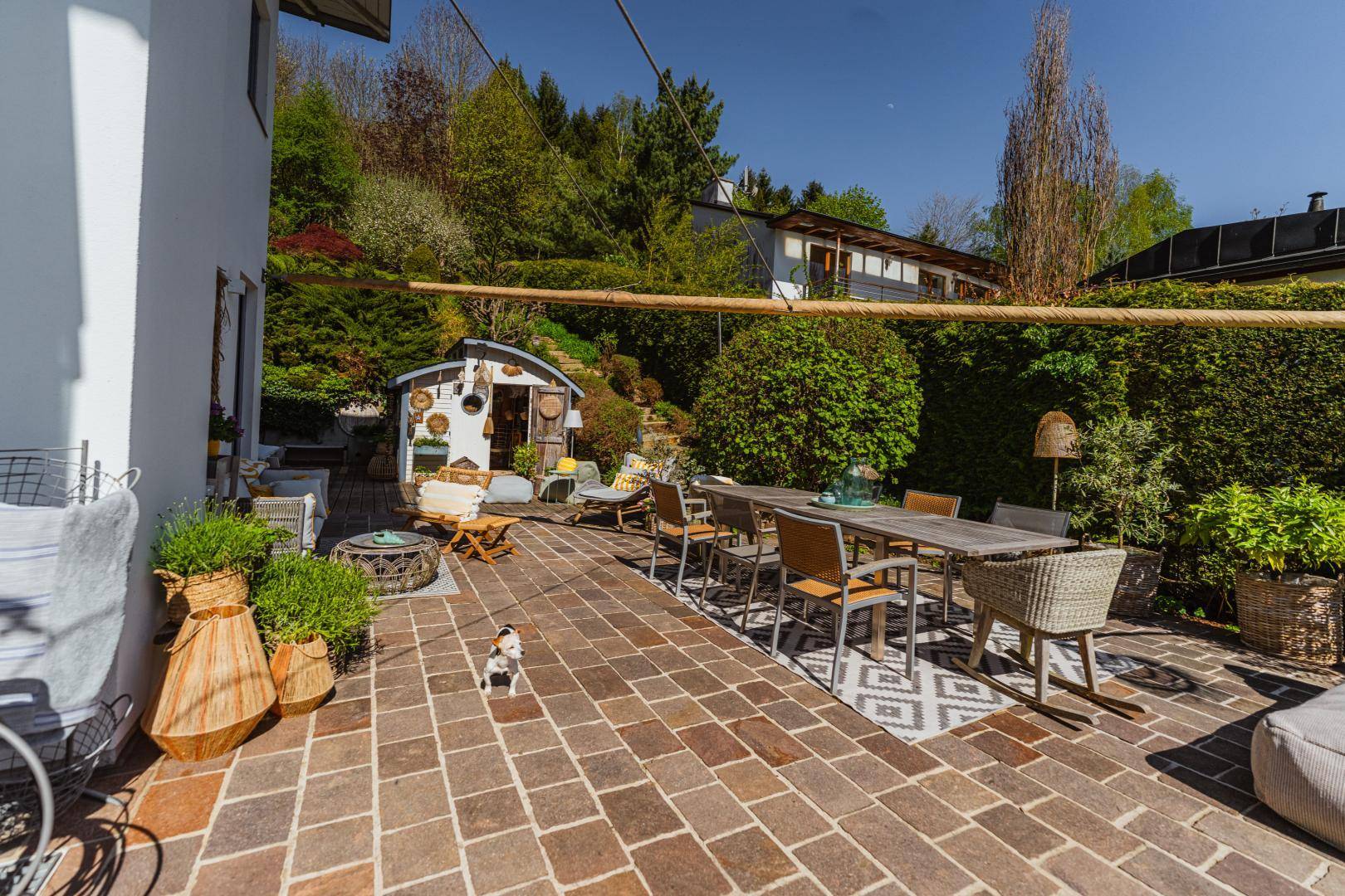 Weitläufige Terrasse mit Ziegelpflaster, Gartenhaus und Blick auf den Poolbereich und die Natur.