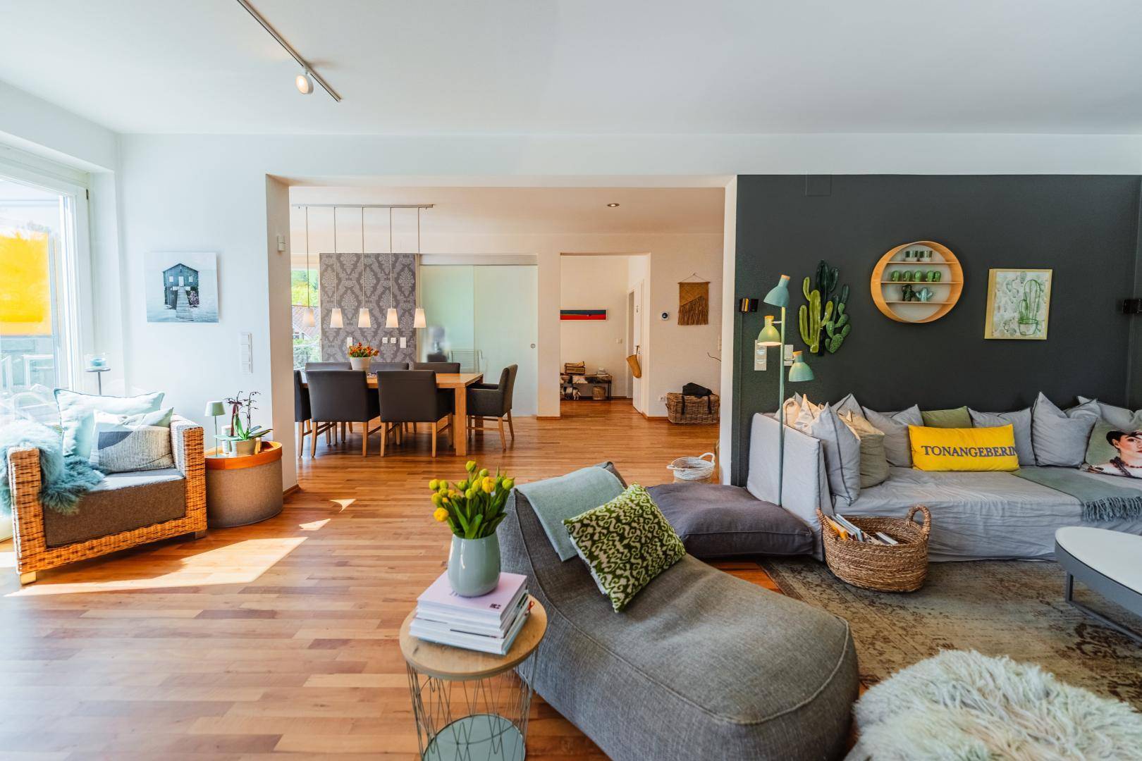 Helles Wohnzimmer mit Holzboden, modernem Sofa und offenem Übergang zum Essbereich.