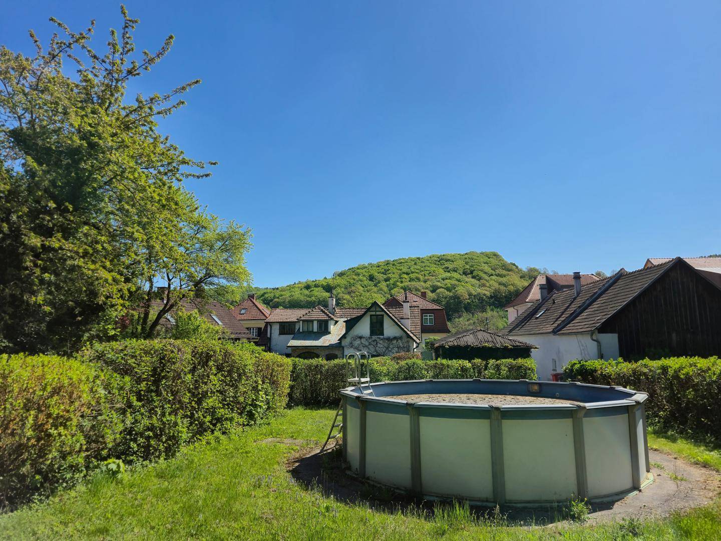 Gartenbereich mit Aufstellpool und Blick auf die umliegende Hügellandschaft und Nachbarhäuser.