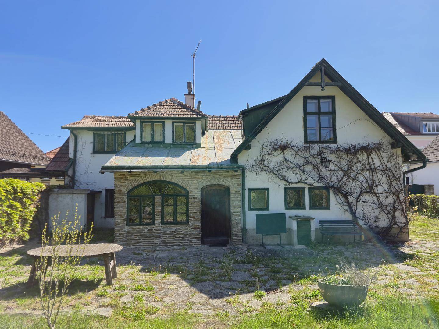 Rückansicht des Hauses mit Steinfassade, begrüntem Gartenbereich und rustikalem Holztisch.