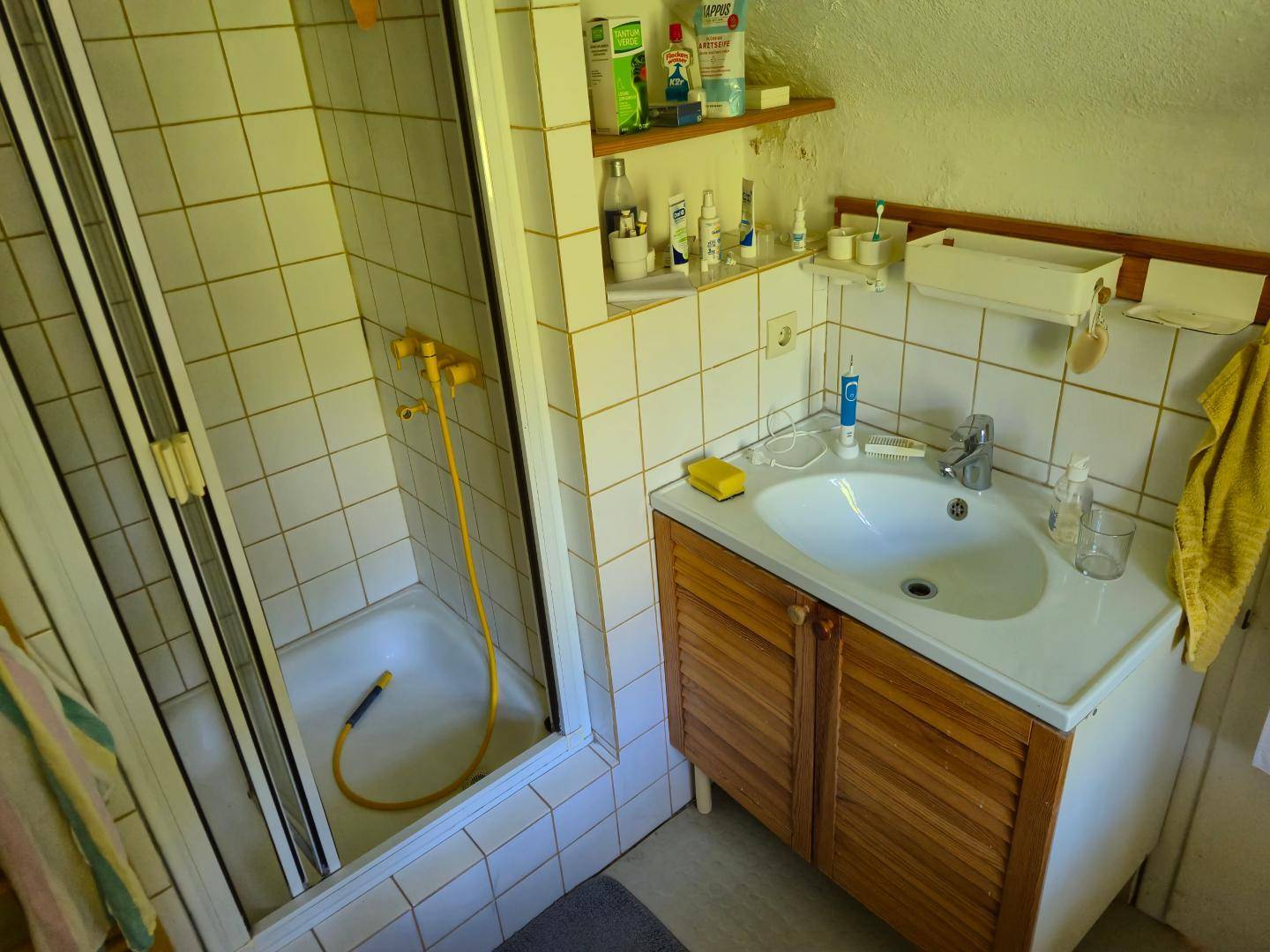 Badezimmer mit Duschkabine, Waschbecken und weißen Fliesen in einem Dachgeschossraum.