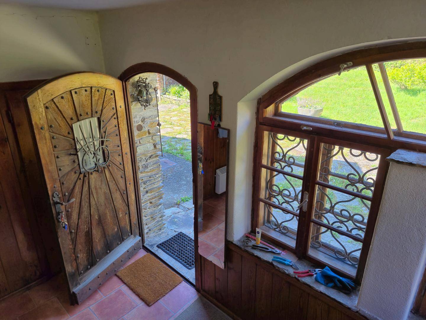 Eingangsbereich mit rustikaler Holztür, schmiedeeisernen Fenstergittern und Terrakottafliesen.