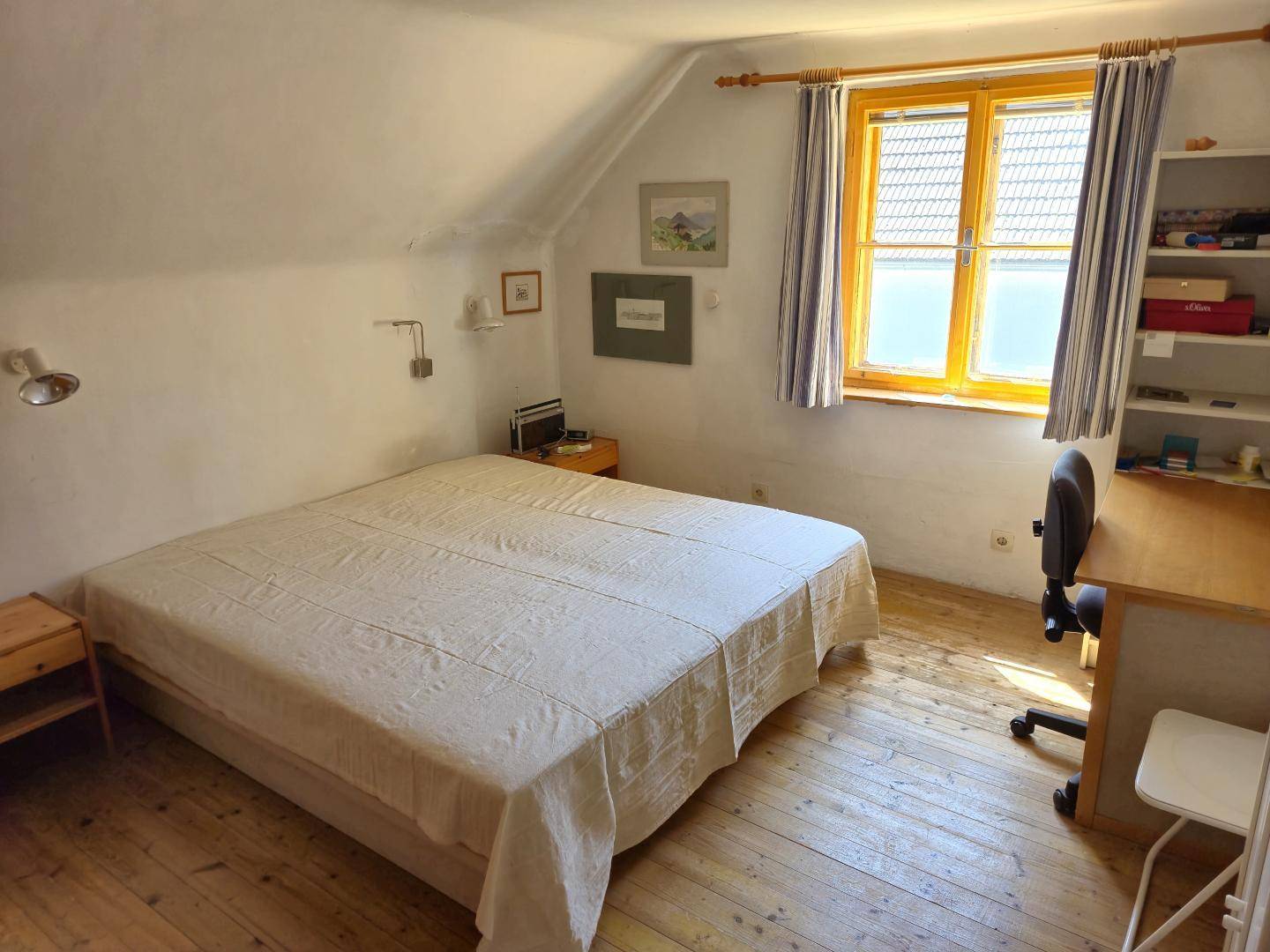 Helles Schlafzimmer im Dachgeschoss mit Doppelbett, Schreibtisch und Holzdielenboden.