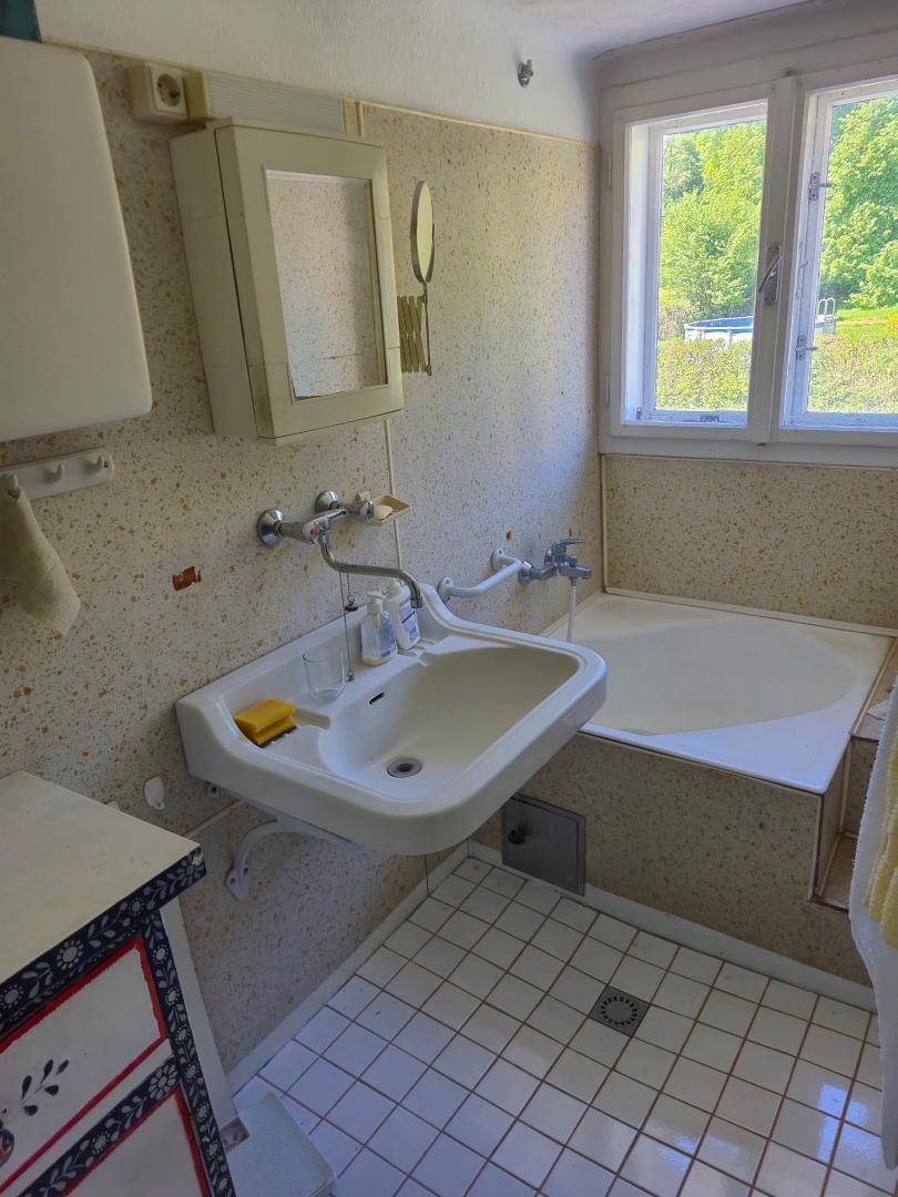 Badezimmer mit Badewanne, Waschbecken und hellen Fliesen, ausgestattet mit einem Fenster.