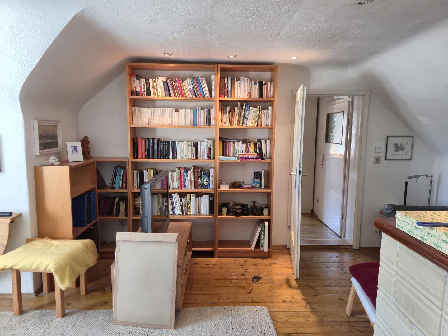 Dachzimmer mit Bücherregalen, Holzdielenboden und Zugang zu einem weiteren Raum.