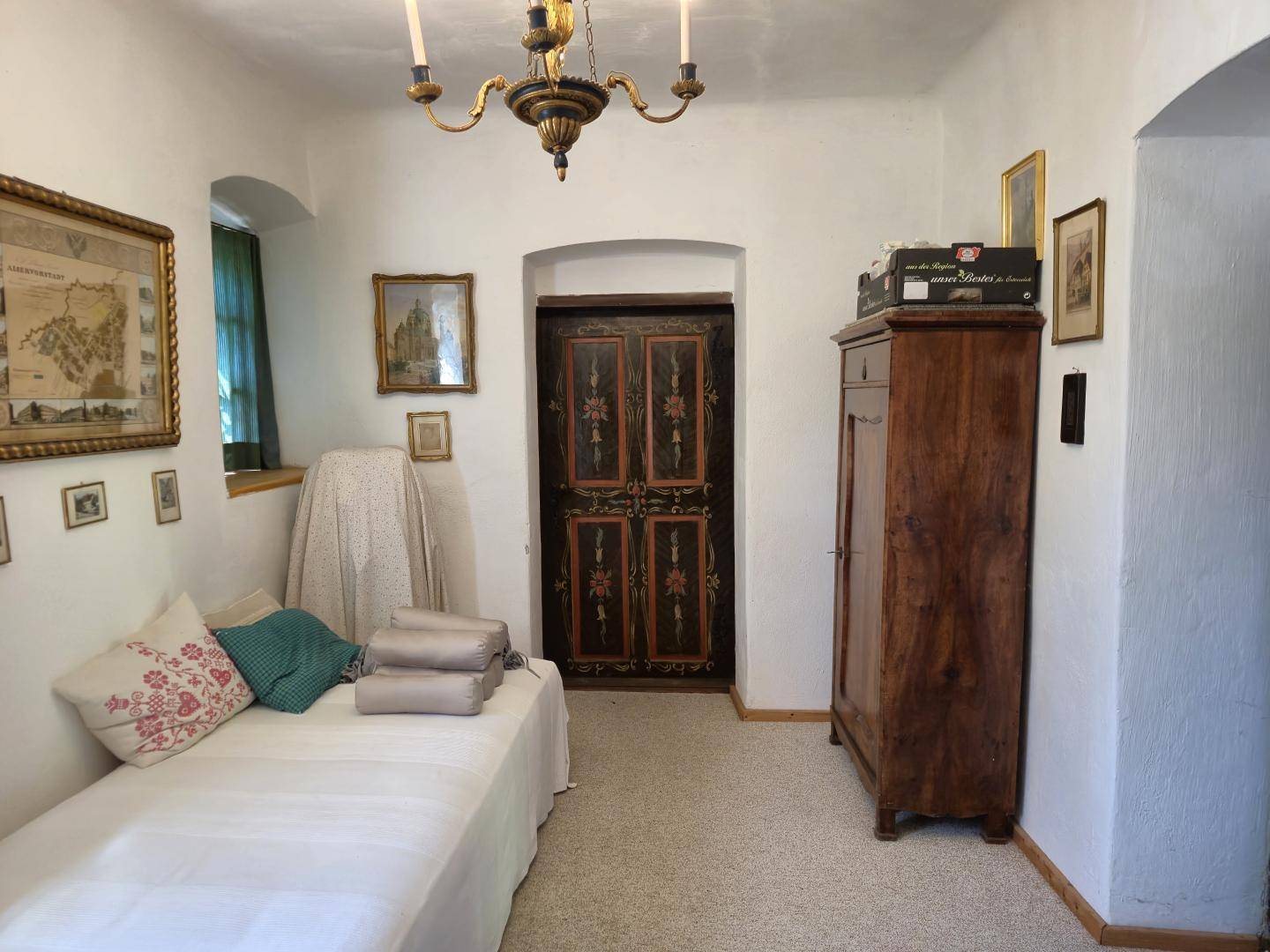 Schlafzimmer mit Einzelbett, antikem Holzschrank und traditioneller Deckenleuchte in hellem Ambiente.