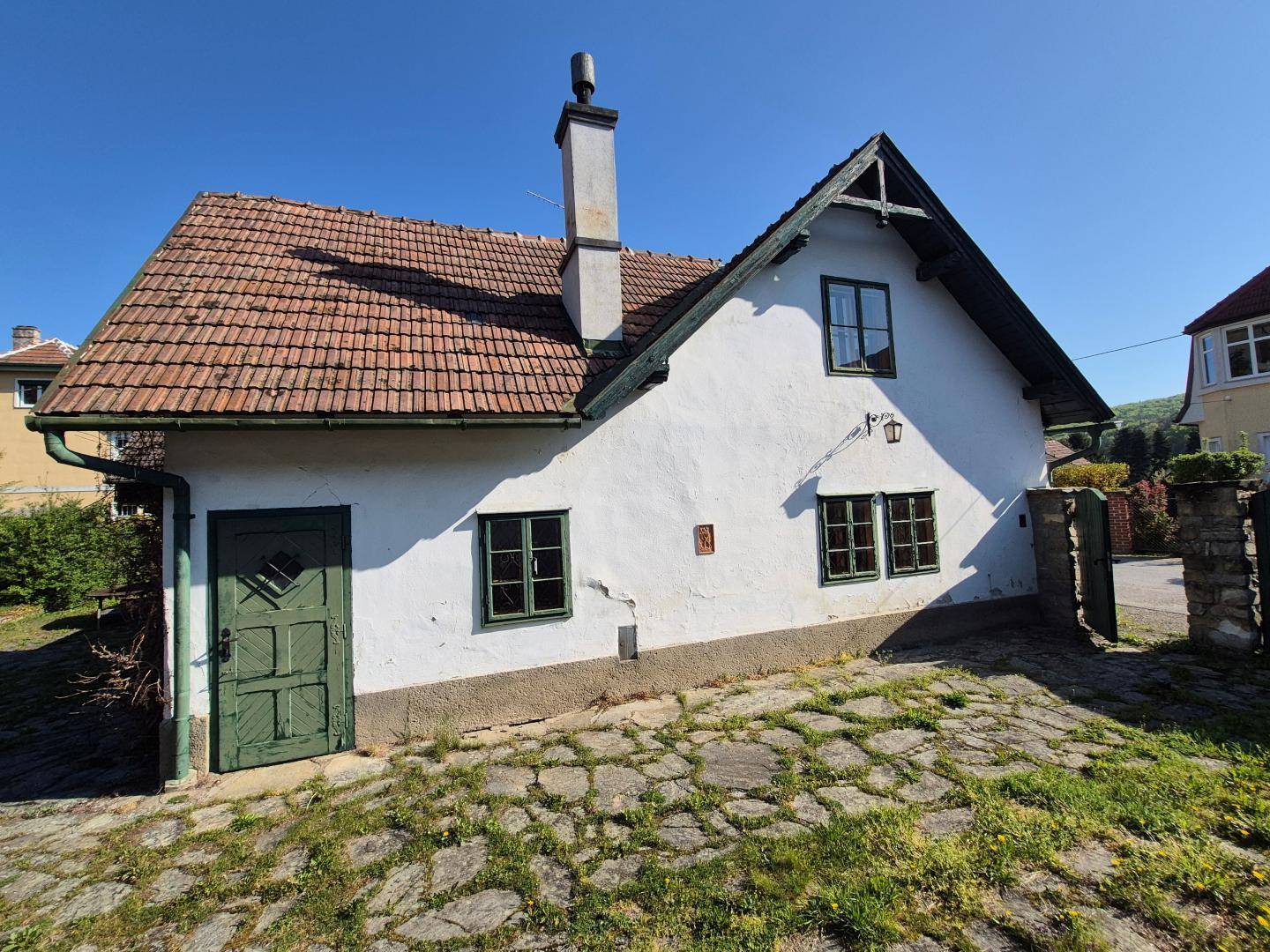 Seitenansicht des charmanten Hauses mit weißer Fassade, grünen Fenstern und traditionellem Ziegeldach.