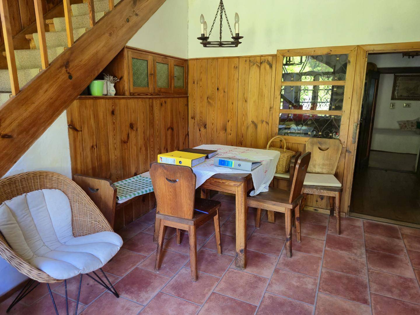Gemütlicher Essbereich mit Holztäfelung, Terrakottafliesen und rustikalen Holzmöbeln unter einer Treppe.
