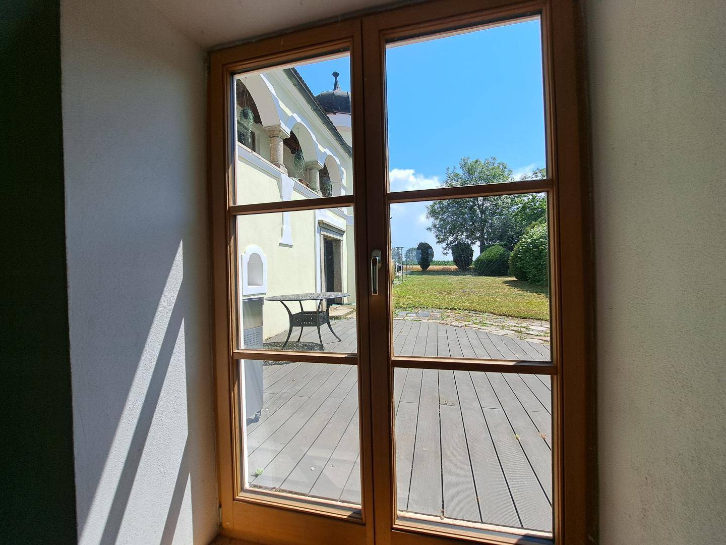 Blick durch die Holztüren auf die Außenterrasse und den grünen Gartenbereich.